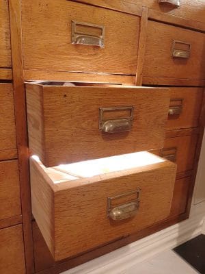 A vintage wooden cabinet with open drawers reveals a bright LED light inside, highlighting metal handles and label slots for rustic charm.