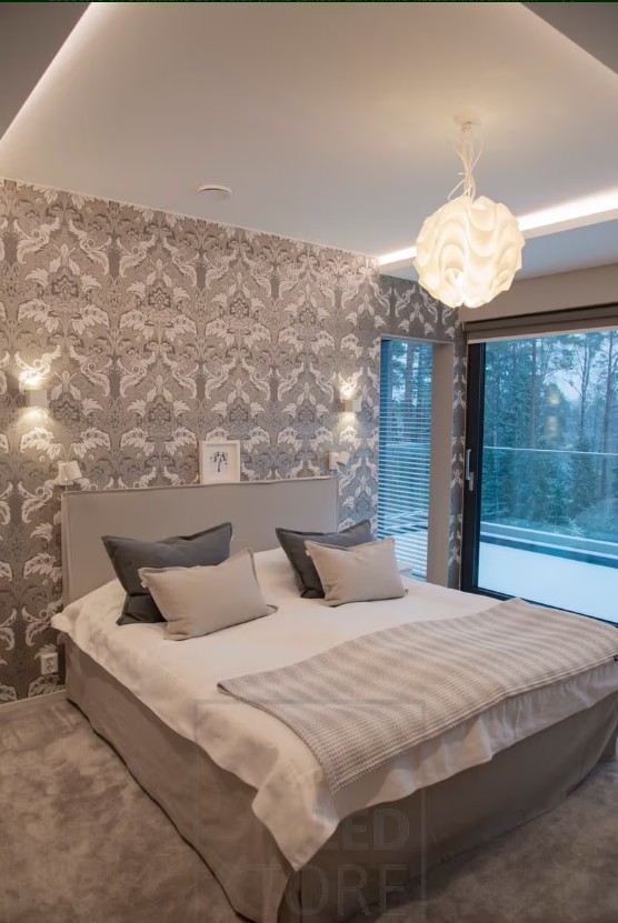 Moderni huone, jossa tyylikäs kuviotapetti, suuri sänky pohjaeilla vuodevaatteilla ja laadukas LED-valaistus LedStore.fi:stä luovat täydellisen tunnelman. Ikkunasta avautuu näkymä lumiseen maisemaan, mikä mukavaee viihtyisän ja rauhallisen ilmapiirin. - LedStore In this bedroom, XL-Cubic wall lights are installed on the wall, along with LED strips in the light cove to create ambiance. The ceiling light adds a decorative touch and provides extra illumination to the room.