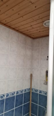 Cozy bathroom with floral tiles, wood ceiling, recessed LED light, casting soft glow. Broom adds charm. White and blue theme; LED lighting focus.