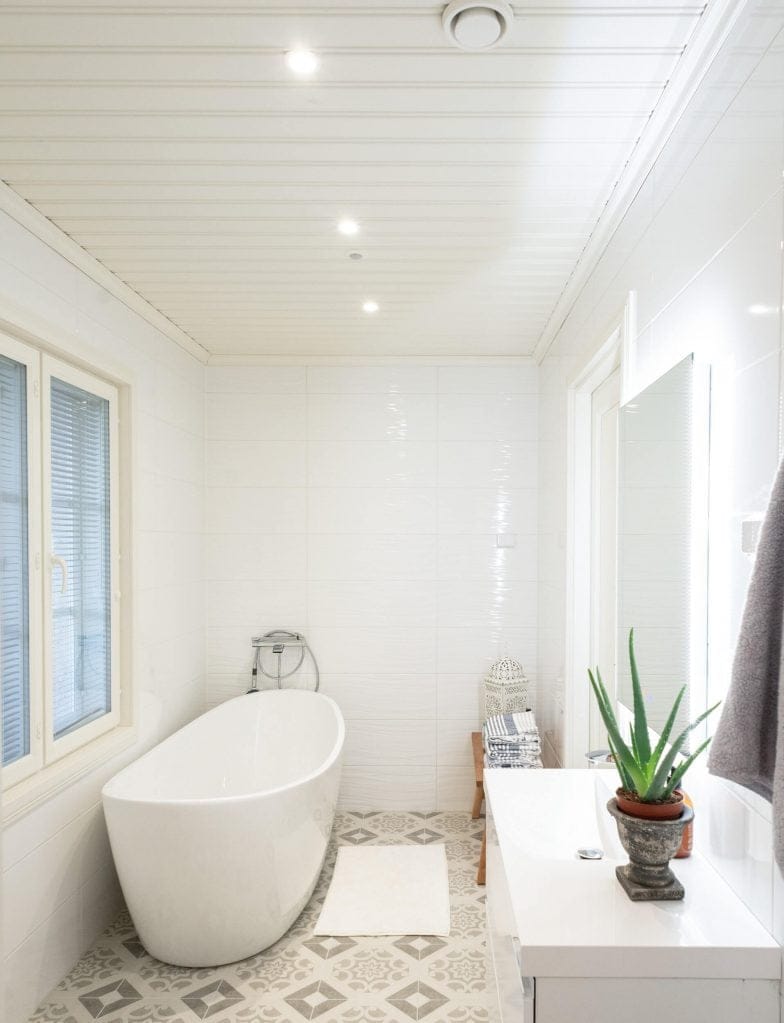 Moderni kylpyhuone LED-valaistuksella; Siinä on vapaasti seisova kylpyamme, pesuallas peilillä ja kasveilla, valkoiset seinät, katto ja kuviollinen laattalattia.