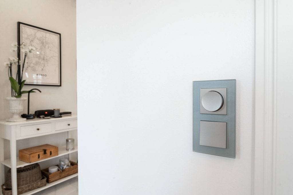 Moderni minimalistinen huone, jossa on LED-valaistu konsoli, tyylikäs valokytkin, koriste-esineitä, ruukkukasvi ja kehystetty kartta valkoisella seinällä.