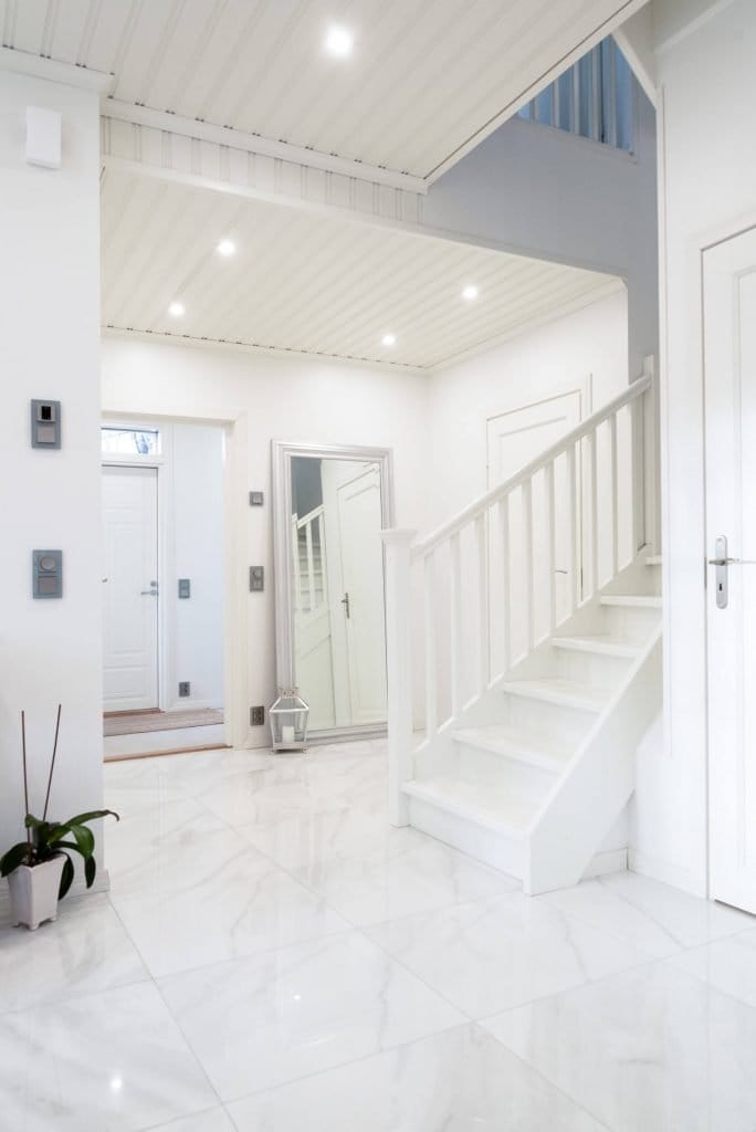 Moderni eteinen, jossa valkoiset marmorilattiat, tyylikäs portaikko, iso peili, ruukkukasvi, valaistu energiatehokkailla LED-uppokattovaloilla.