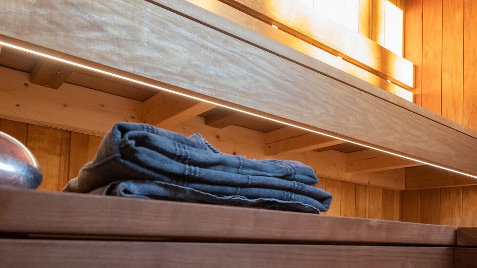 Farkut taiteltuna puisella penkillä valaistussa, puupaneelien reunustamassa huoneessa tunnelmallisessa LED-valossa.