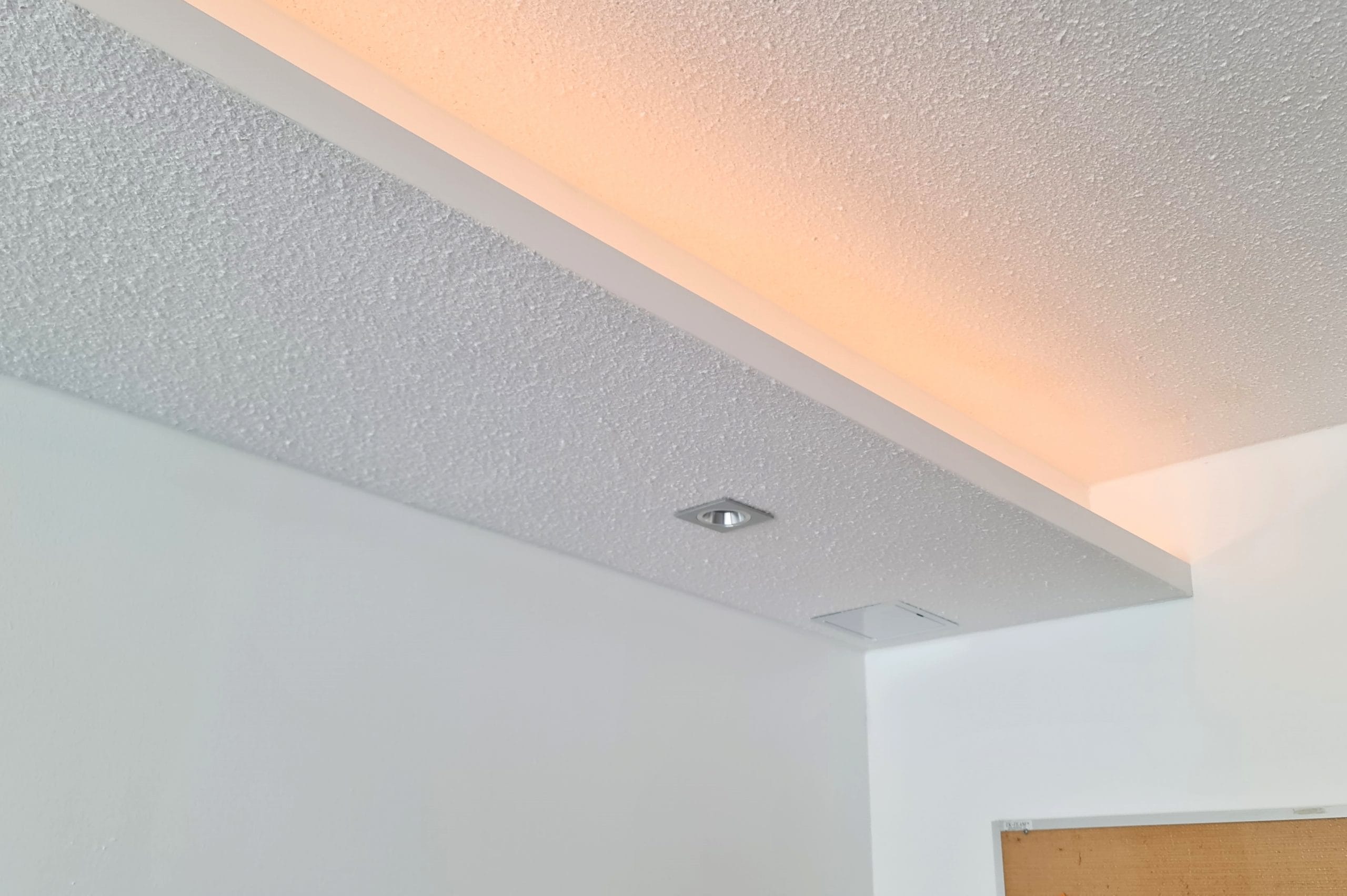 LedStore.fi verkkokauppa tarjoaa tyylikkään teksturoidun katon, johon on upotettu pehmeää ja epäsuoraa LED-valaistusta, luoden lämpimän hehkun tilaan. Kattoon on asennettu pieni, neliönmuotoinen hopeinen valaisin korostamaan modernia ilmettä. Alaoikealla näkyy osa tyylikkäästä puuovesta, täydentäen kokonaisuutta.