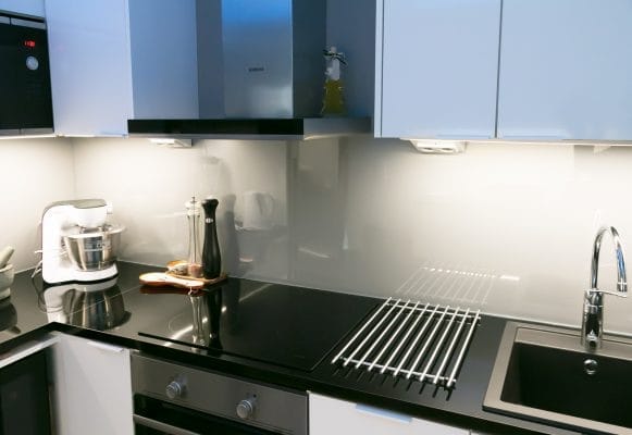 Modern kitchen with LED under-cabinet lighting, black countertops, white cabinets, blender, salt and pepper grinders, stove, metal drying rack.