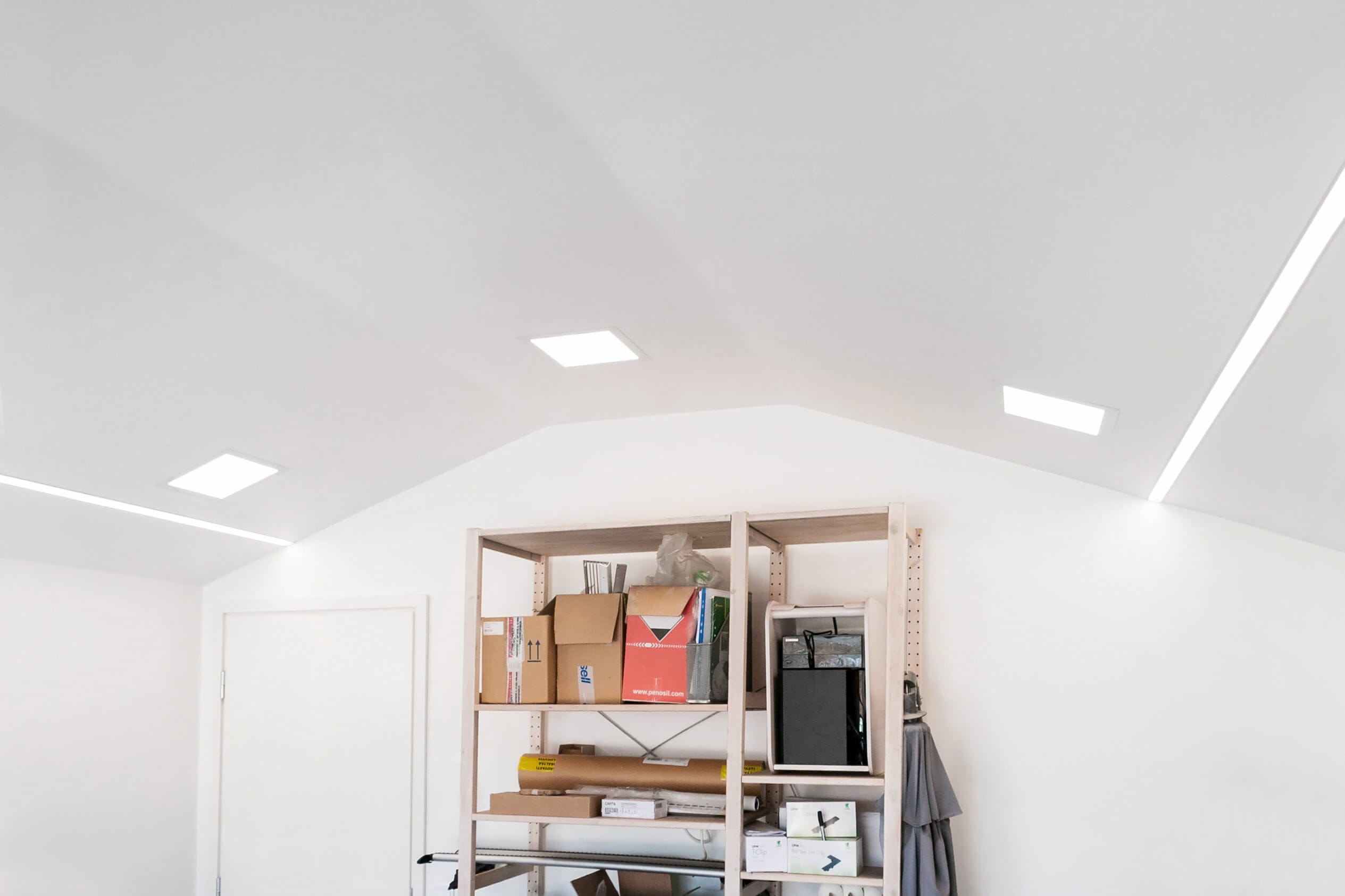 Figure 4. Garage warehouse lighting - LedStore Minimalist room with white ceiling and LED recessed lighting, featuring a tall shelving unit with boxes and clothing displayed for a modern look.
