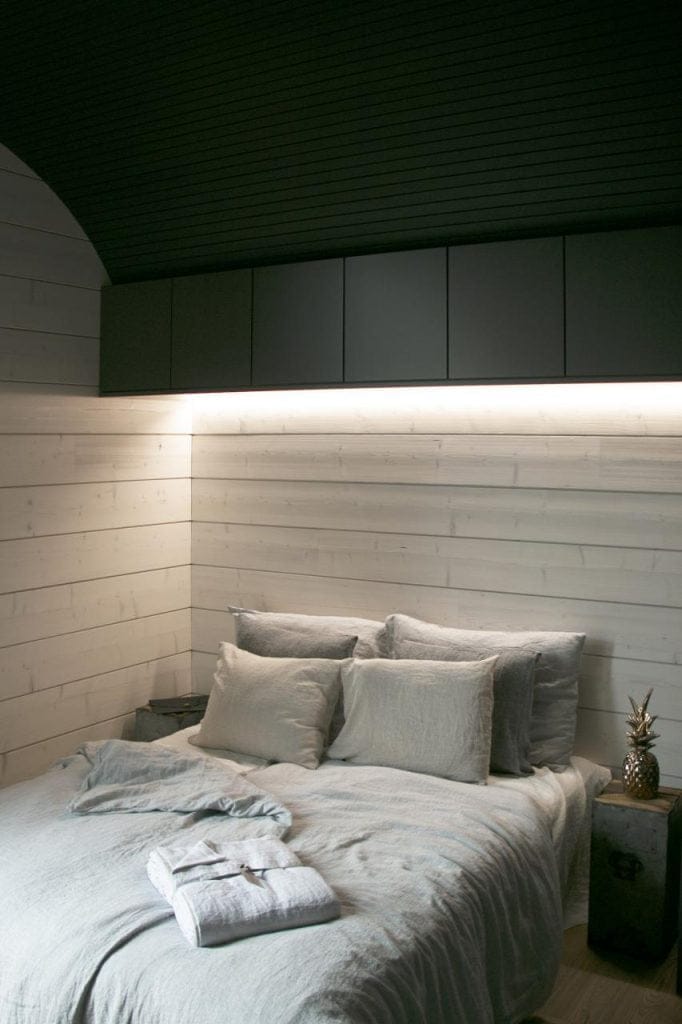Led ribbon in alcoves - LedStore Luo viihtyisä ja moderni makuuhuone LedStore.fi:n LED-valaistuksen avulla. Huoneen keskipisteenä on siististi pedattu sänky, jossa on vaaleanharmaat lakanat ja useita tyynyjä. Sängyn yläpuolella on tyylikkäät, tummat kaapit osana puupaneloituja seiniä, ja pehmeä LED-valaistus luo lämpimän tunnelman. Vuoteella lepää huolellisesti viikattu kylpytakki.