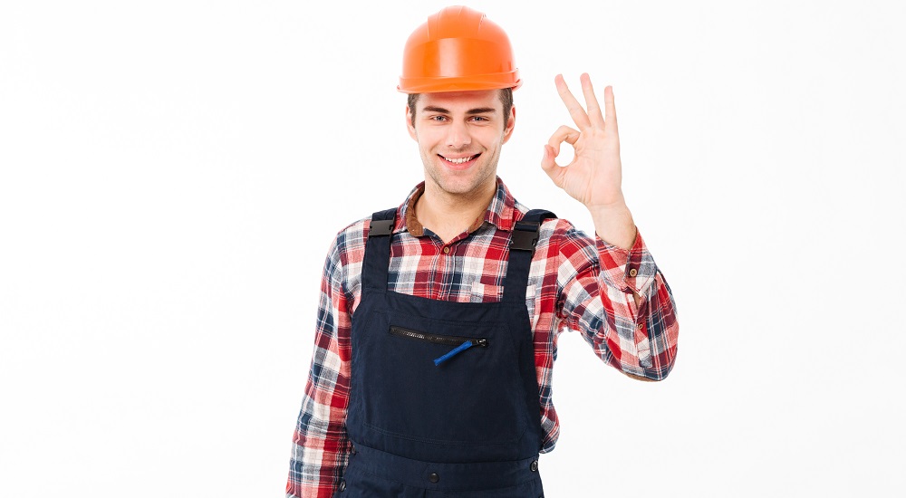 Porträtt av en glad ung manlig byggare som visar tummen upp-gest medan han står och tittar på kameran isolerad över vit bakgrund.