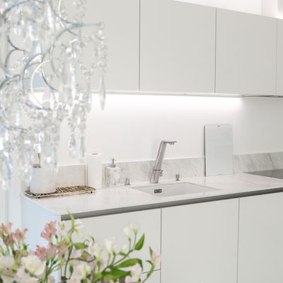 Modern white kitchen with marble worktops, under cabinet LED lighting, crystal chandelier and pink floral decorations in the foreground.
