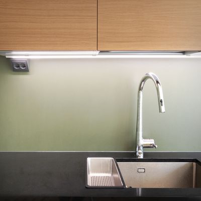 LED illuminated kitchen sink area, chrome faucet, black countertop and light green backlighting under cabinet.