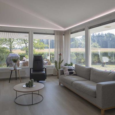Modern living room with LED ceiling lights, floor lamp, natural light from large windows, comfortable seating.