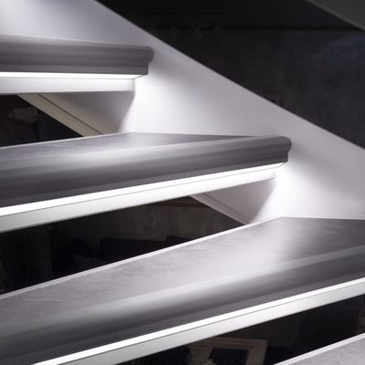 A detailed view of a floating staircase with a stylish LED lighting fixture, accent lighting and a white wall.