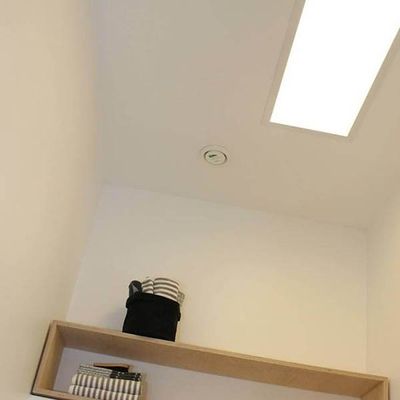 Cozy room with wooden shelf, striped blanket, basket, books. An accent LED ceiling light and smoke alarm for modern home security and style.