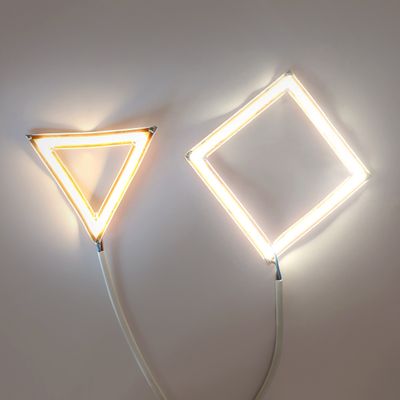 Wall mounted LED tube lights, triangular and diamond shaped, visible power cord, ambient lighting.