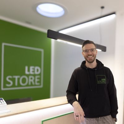 A man in LED STORE-huvtröja vid belysningsdisk, green LED-skylt, modern boutique environment