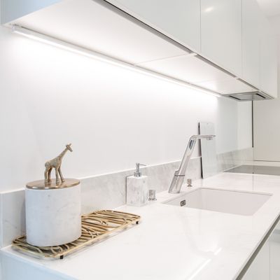 Modern kitchen with white worktop, silver faucet, giraffe figure in tank; bright LED lighting under cabinets for more space.