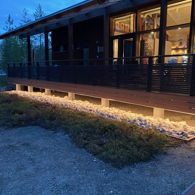 A modern wooden building with an LED-lit porch amidst rocks, twilight skies and trees - for more evening ambience and energy efficiency.