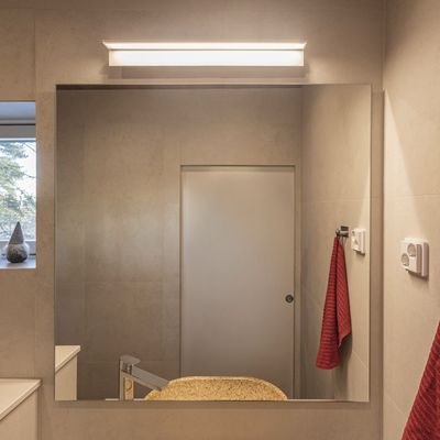 Modern bathroom with energy efficient LED lighting, large mirror, beige countertop, stylish faucet and red towel hook for a stylish interior.