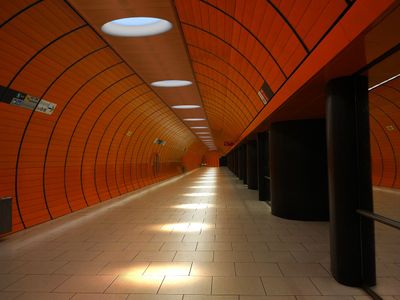Empty, well-lit orange metro station with tiled floor, black columns, curved tunnel design and wall signs