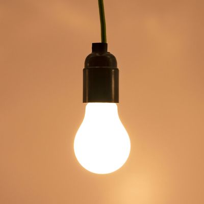 LED lamp with green wire, glows warmly against a brown background. Ideal for energy-efficient lighting solutions and to enhance the atmosphere.