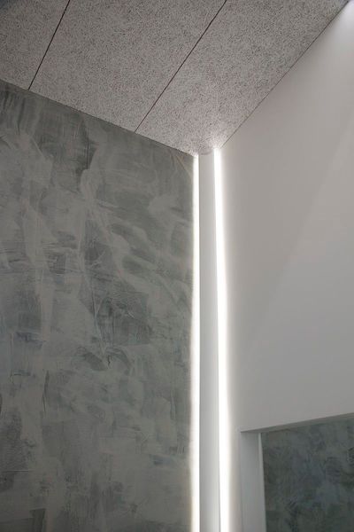Modern corner interior with textured grey walls and vertical LED strip lights; minimalist and bright.