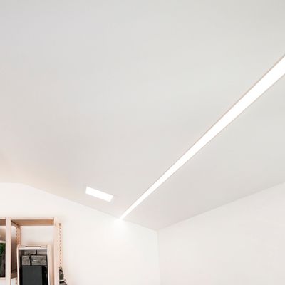 A modern room with a sloping ceiling, stylish recessed linear LED lighting and corner shelves with a variety of decorative products.
