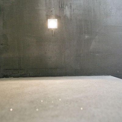 A minimalist room with grey walls and floor, with a small square LED light on the back wall.