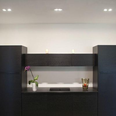 Minimalist black bathroom with LED lighting, small sink, orchid with white pot on the left, glass candlestick on the right for elegance and style.