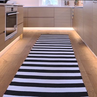 Modern kitchen with wooden cabinets, oven and black and white carpet on wooden floor, illuminated by LED lighting.