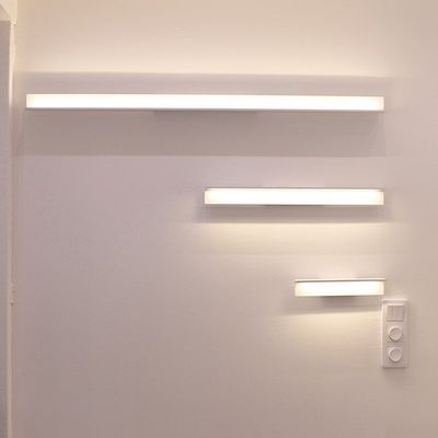 Three increasing sizes of horizontal rectangular wall lights on a white wall, with a light switch under the smallest one. Modern LED lighting design.