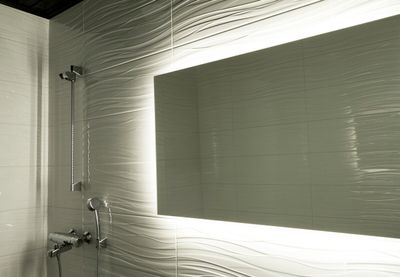 The modern bathroom features textured white tiles, a large backlit mirror and a sleek silver shower head and faucet with stylish LED lighting.