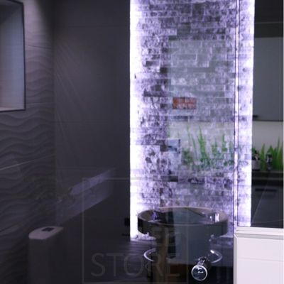 Modern bathroom with textured tiles, backlit wall, circular sink and mirrored illuminated tiles. Elegant LED lighting showcases the luxurious design.
