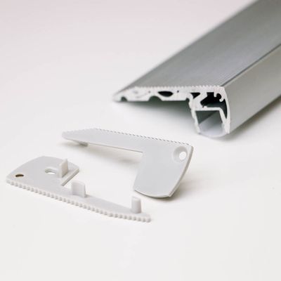 Close-up of dismantled LED lighting components: grey metal track and white plastic parts with a toothed edge. High quality LED lights for sale.