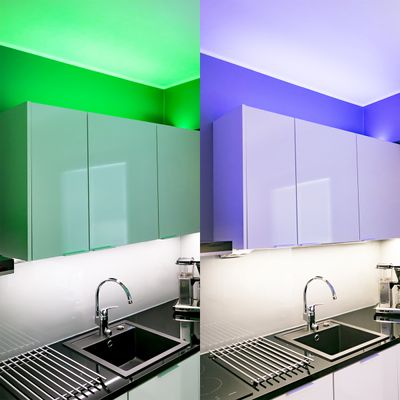Modern kitchen with glossy cabinets and black sink, dynamic LED lighting: vivid greens on the left, rich purples on the right.