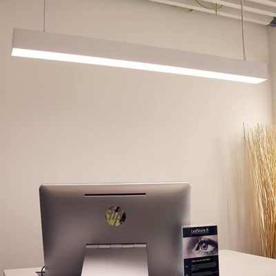 A stylish LED desk lamp that illuminates a modern office with a computer on a white desk; decorative branches in a tall vase in the background.