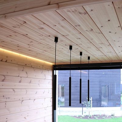 A modern interior with wooden walls and ceiling, four black pendant lights and a large window facing the garden.