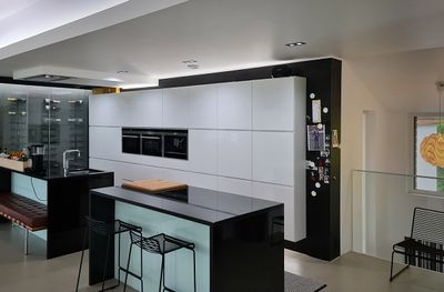 Modern kitchen with gloss white cabinets, black countertops, island with bar stools, stainless steel double oven, refrigerator with magnets right under LED lighting.
