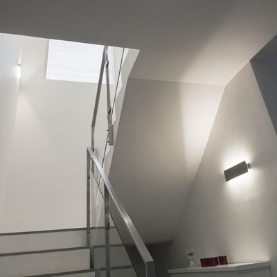 Modern staircase with metal railing, grey walls and LED wall lighting leading to a small window above - energy efficient lighting.