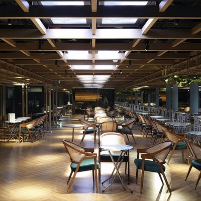 Modern indoor restaurant with wooden floors, tables, chairs lined up under a lattice roof with skylights enhanced by atmospheric LED lighting.