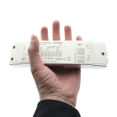 In the hand, a white rectangular device displaying technical information and symbols and the word "Zigbee" associated with LED lighting technology.