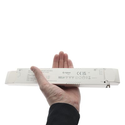 Close-up of a hand holding a rectangular Zigbee LED controller, displaying several printed certificates and symbols for quality assurance.
