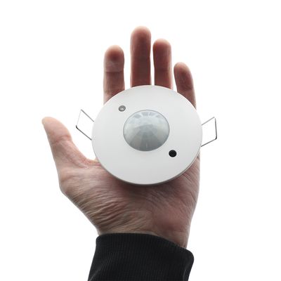 Hand-held round white motion sensor with central knob, two metal clips; ideal for energy-efficient LED lighting automation.