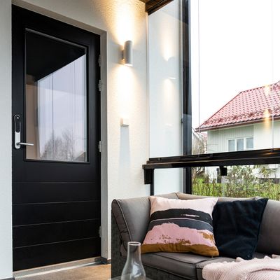 Modern sunroom with energy efficient LED lighting, black door, grey sofa with colourful cushions, glass walls showcasing the house with a vibrant red roof.