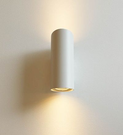 A stylish cylindrical LED wall light illuminates warm beams of light up and down a white wall; ideal for modern, minimalist interiors.