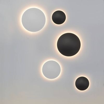Five modern round wall lamps, three black and two white, radiate a warm light against a light background. Stylish LED lighting for contemporary interiors.