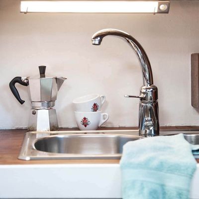Modern countertop sink with chrome tap, moka pot, overlapping cups with red logo, light blue towel on counter - the perfect place for energy efficient LED lighting.