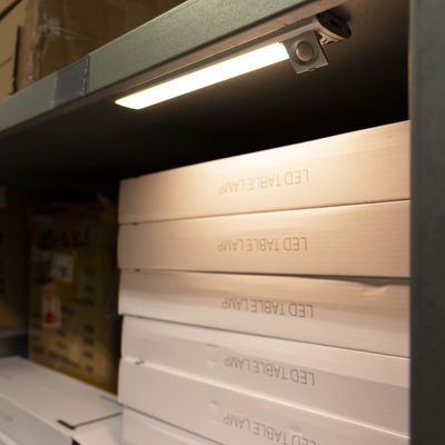 Close-up of a storage shelf with overlapping white drawers marked "LED TABLE LAMP" and illuminated by a small overhead light - LED lighting company.