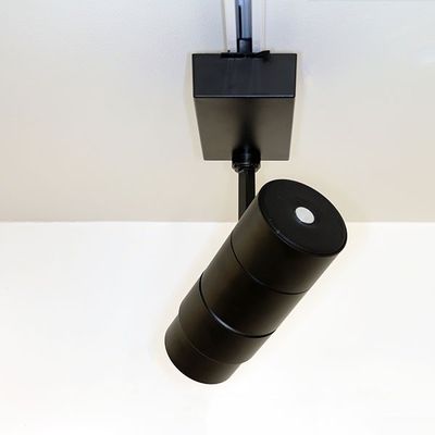 Modern black cylindrical LED luminaire for white ceiling, mounted on a stylish black rail system for versatile lighting solutions.