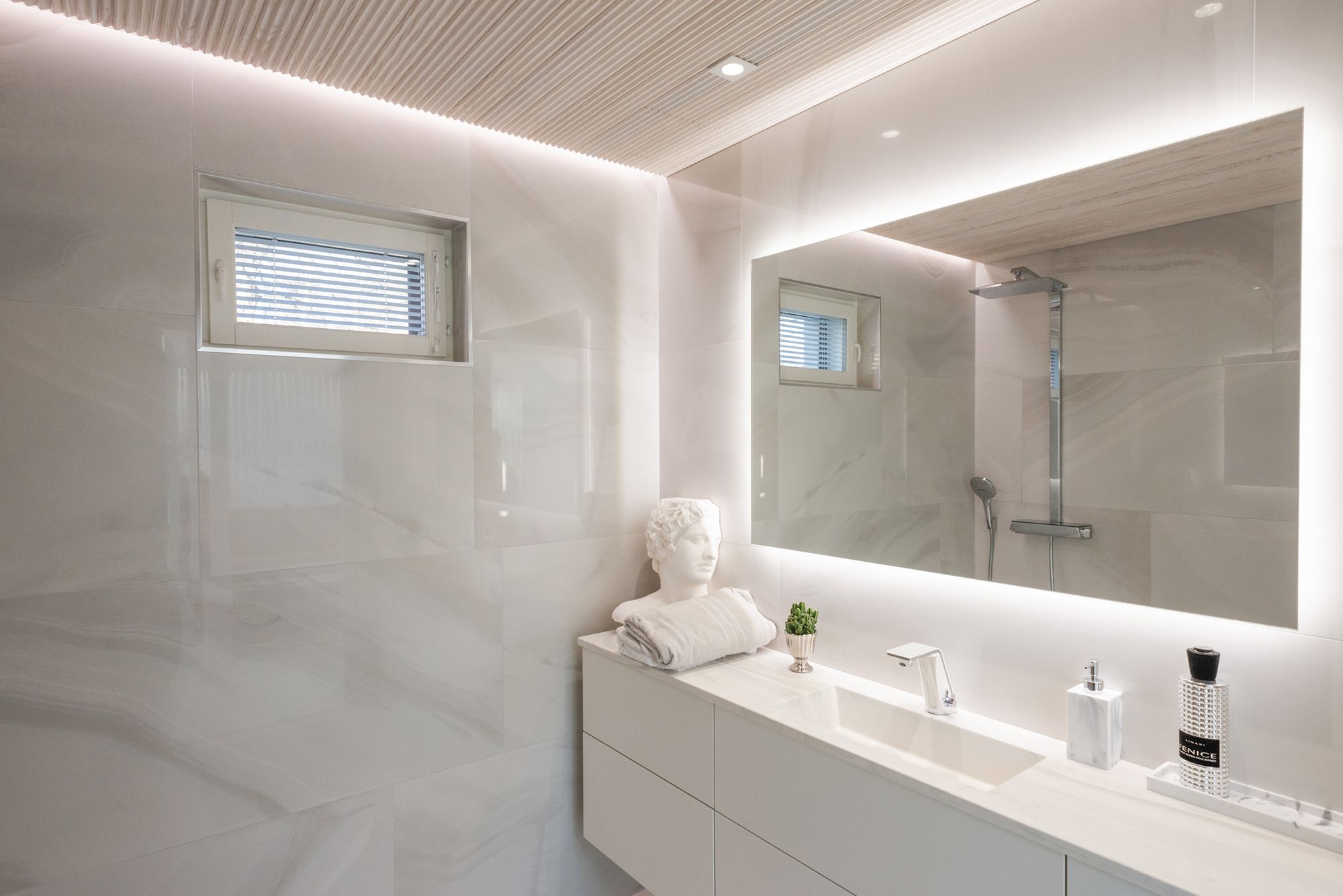 In a bathroom with a spa bath, a large, space-consuming light mirror combined with spotlights and a wall-to-ceiling LED strip.