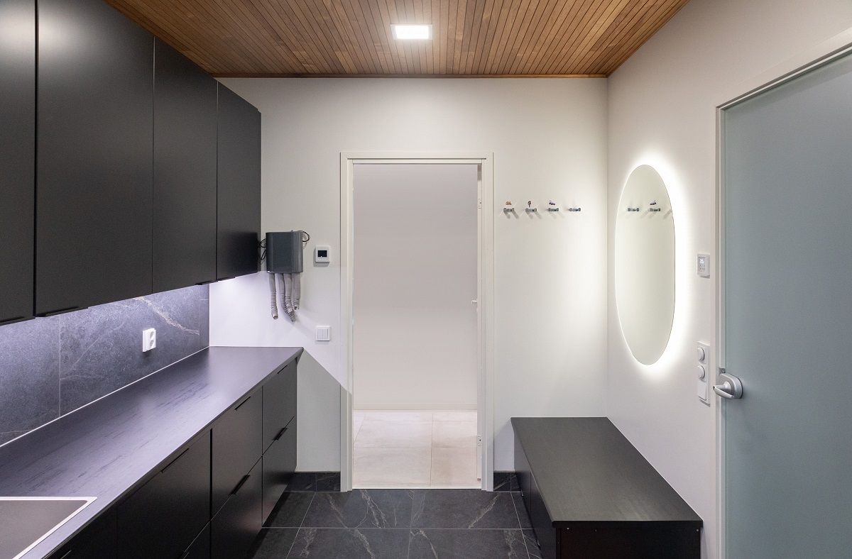 In the ceiling of a home care room, a small rectangular panel lamp, an oval mirror and an LED strip illuminate the worktop.